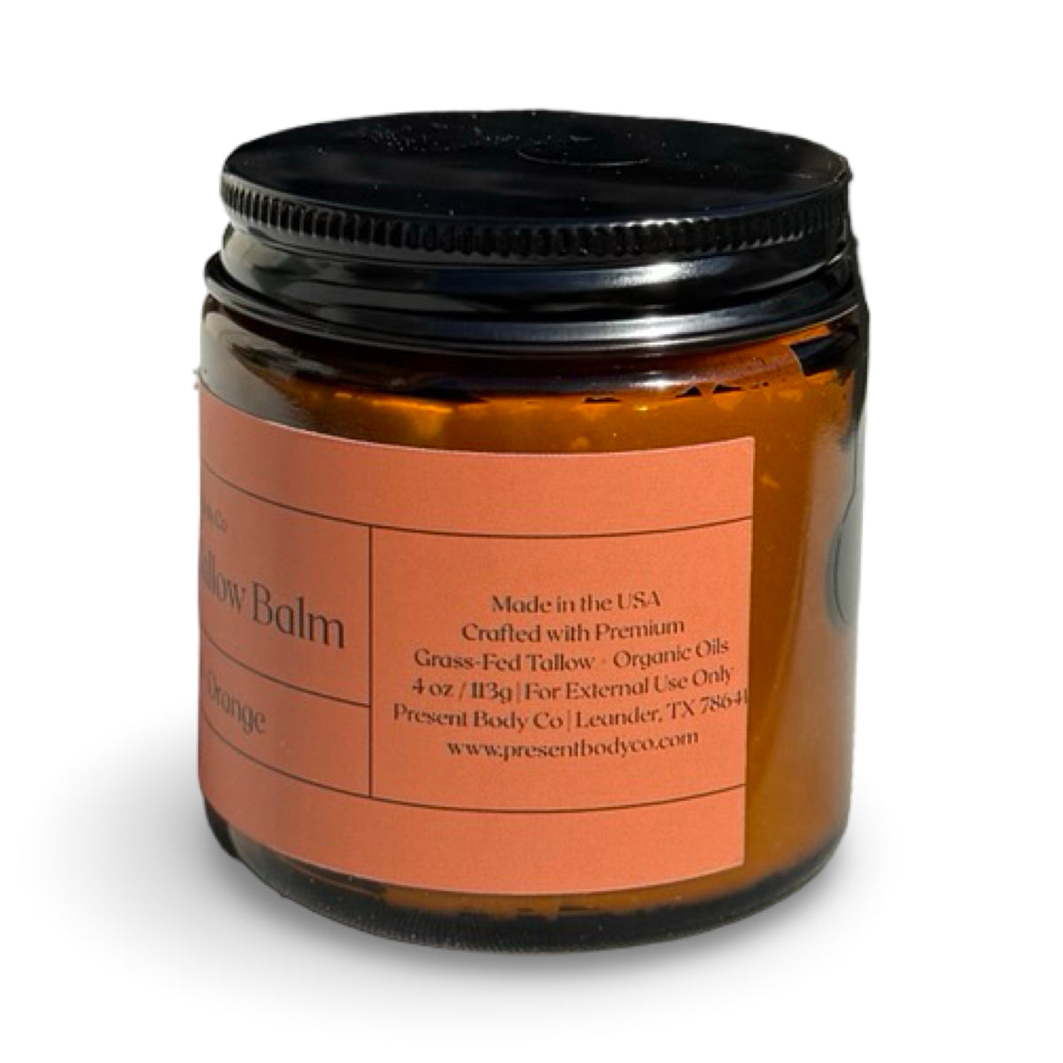 An amber glass jar of Present Body Co. Patchouli + Orange Whipped Tallow Balm with a black lid and a terracotta-colored label, shown on a white background.