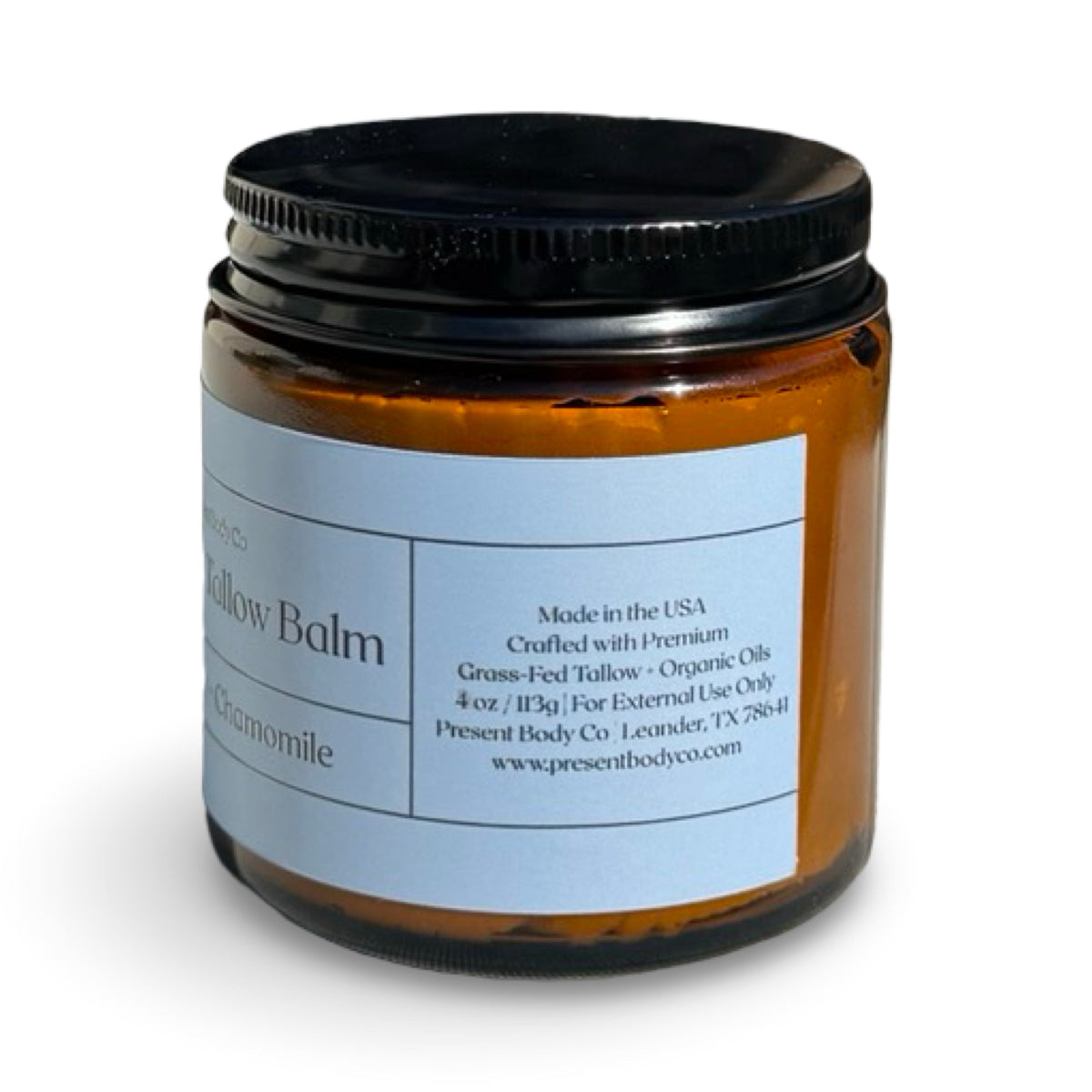 An amber glass jar of Present Body Co. Blue Tansy + Chamomile Whipped Tallow Balm with a black lid and a light blue label, shown on a white background.