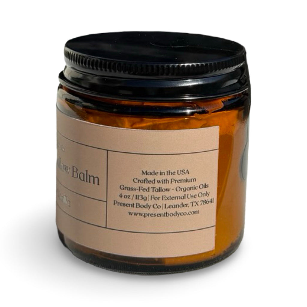 An amber glass jar of Present Body Co. body balm with a black screw-on lid and a beige paper label, shown on a white background.