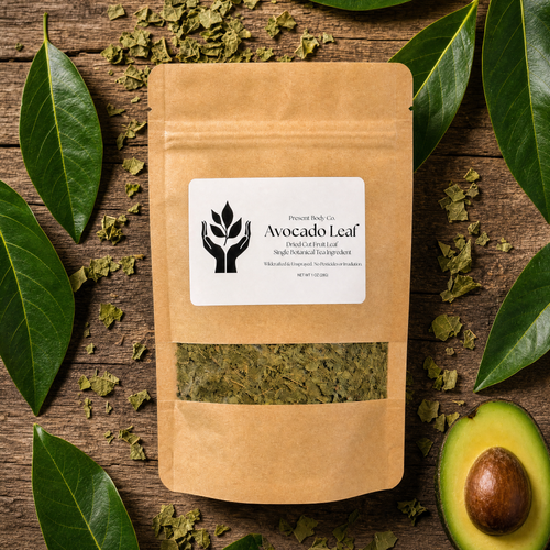 A kraft paper stand-up pouch labeled 'Avocado Leaf' by Plant Based Co., placed on a rustic wooden surface with scattered dried green leaves, whole and halved avocados, and glossy green leaves around it.