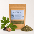 A kraft paper stand-up pouch labeled 'Balance' by Desert Botany Co, shown on a clean white background with fig leaves, figs, and a small pile of dried green herbs in front.