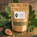 A kraft paper stand-up pouch labeled FigLeaf, filled with dried green leaves, displayed on a rustic wooden board with fresh fig leaves and a sliced fig.