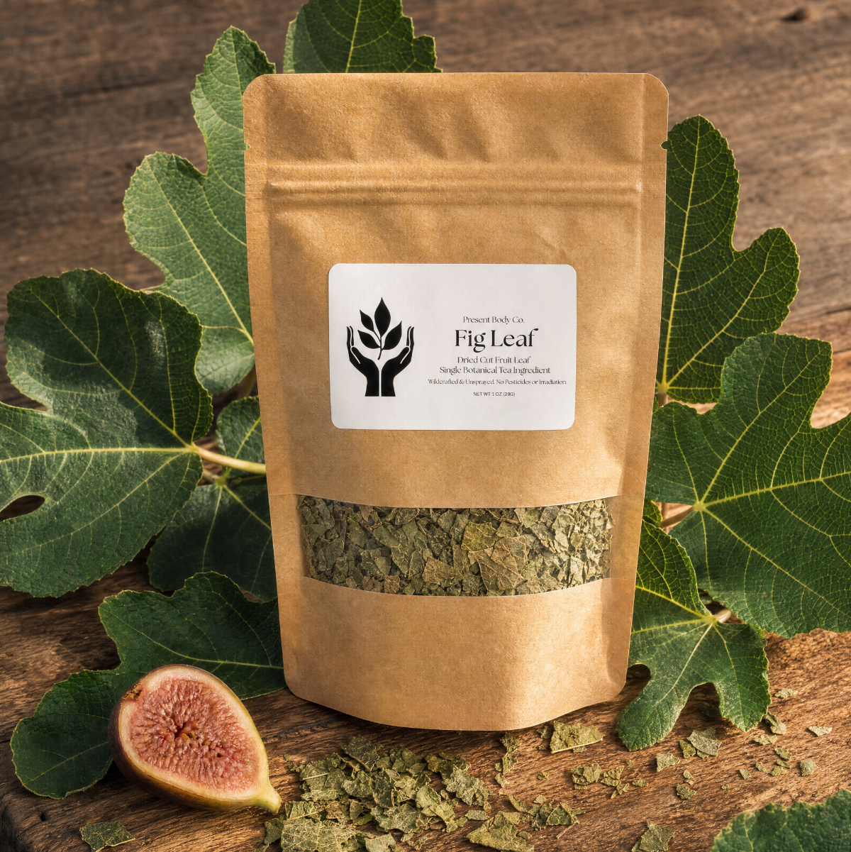 A kraft paper stand-up pouch labeled FigLeaf, filled with dried green leaves, displayed on a rustic wooden board with fresh fig leaves and a sliced fig.