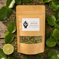 A kraft paper stand-up pouch labeled 'Lime Leaf' with a clear window showing dried green leaves inside, arranged on a rustic wooden surface surrounded by fresh green leaves and a lime slice.