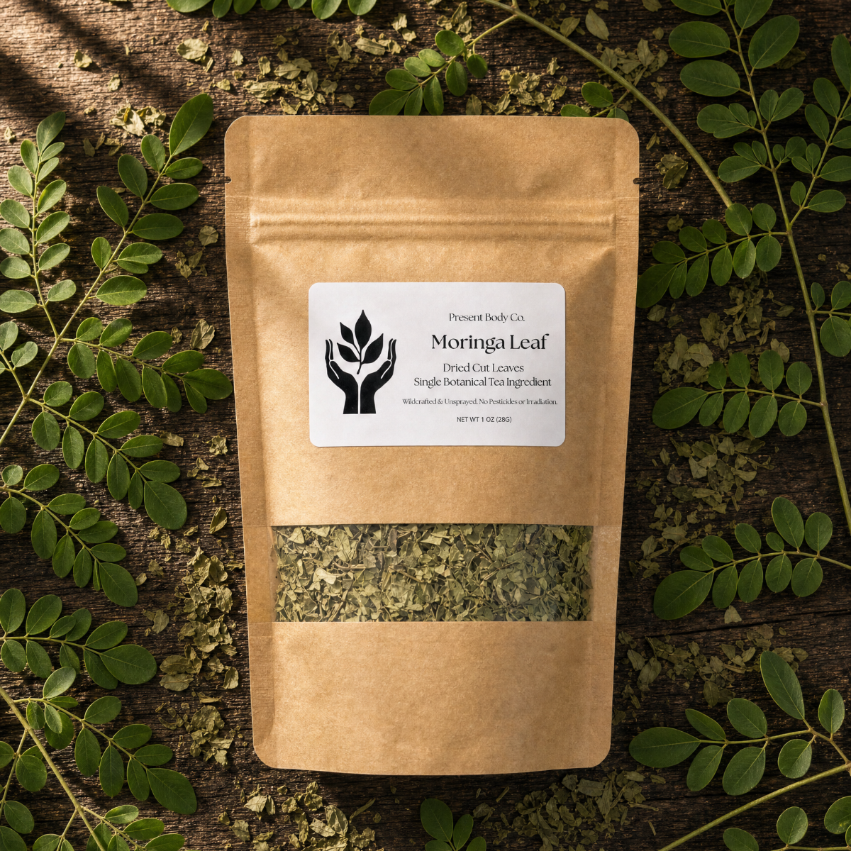 A kraft paper stand-up pouch labeled 'Moringa Leaf' by Moringa Leaf Co., placed on a dark wood surface surrounded by fresh green moringa leaves.