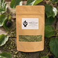 A kraft paper stand-up pouch labeled 'Mulberry Leaf' with a clear window showing dried green leaves, arranged on a rustic wooden surface with fresh green leaves and berries around it.