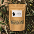 A kraft paper stand-up pouch labeled 'Olive Leaf' by Prairie Herb Co., surrounded by olive branches and olives on a rustic wooden surface.