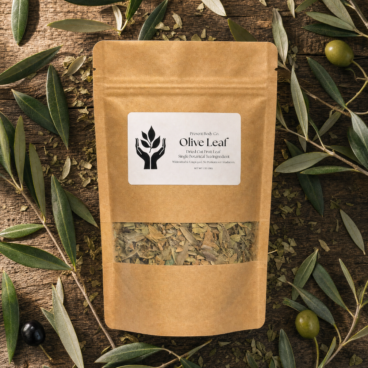 A kraft paper stand-up pouch labeled 'Olive Leaf' by Prairie Herb Co., surrounded by olive branches and olives on a rustic wooden surface.