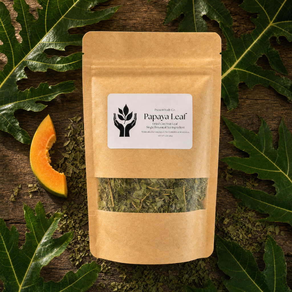 A kraft paper stand-up pouch labeled 'Papaya Leaf' with a clear window showing dried green leaves inside, styled on a dark wood surface with papaya slices and large green leaves around it.