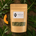 A kraft paper stand-up pouch labeled 'Papaya Leaf' with a clear window showing dried green leaves inside, styled on a dark wood surface with papaya slices and large green leaves around it.