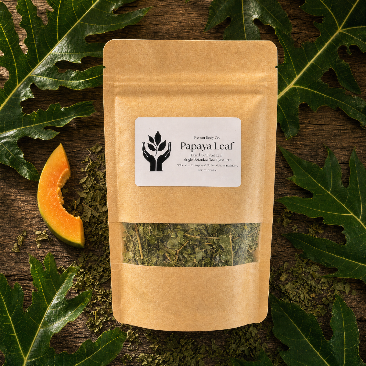 A kraft paper stand-up pouch labeled 'Papaya Leaf' with a clear window showing dried green leaves inside, styled on a dark wood surface with papaya slices and large green leaves around it.