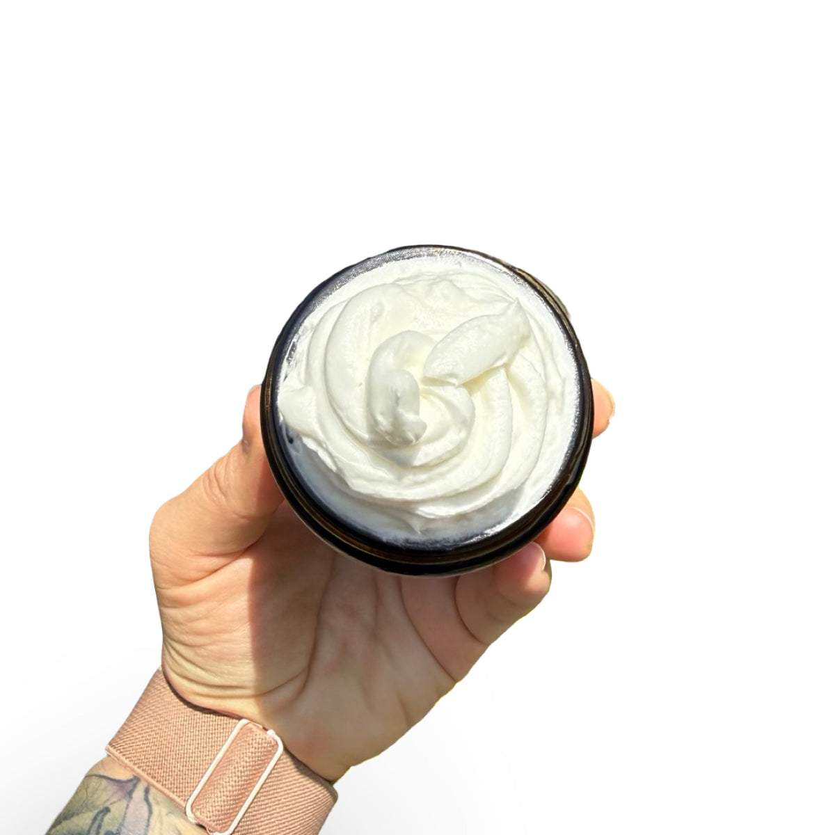 A hand holding an open round black jar filled with whipped white cream against a plain white background.