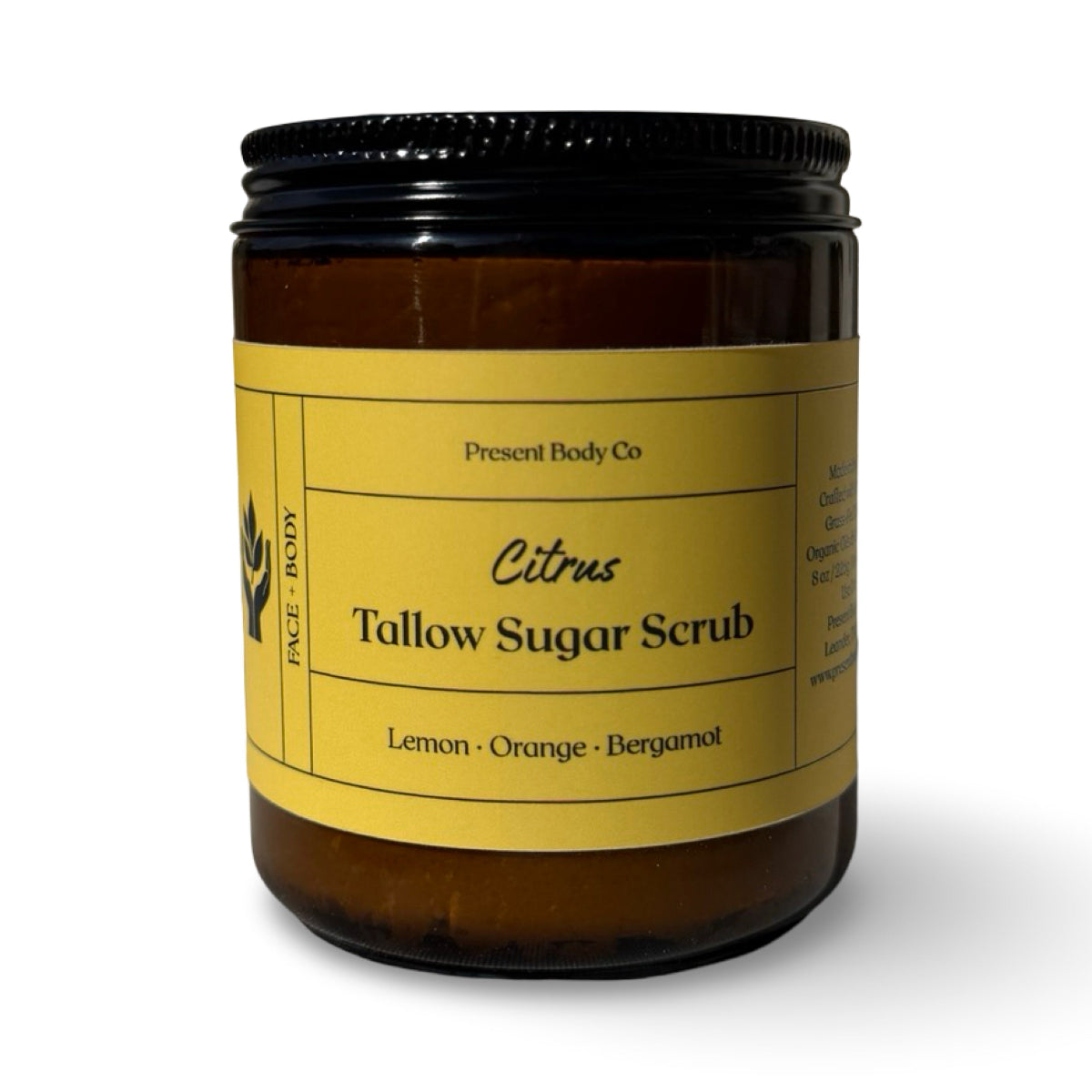 An amber glass jar of Present Body Co. Citrus Tallow Sugar Scrub with a yellow label and a black screw-on lid, set against a plain white background.