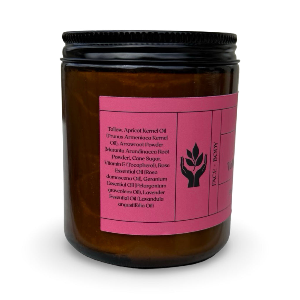 An amber glass jar of Present Body Co. Floral Tallow Sugar Scrub with a black metal lid and a bright pink label, photographed on a clean white background.