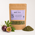 A kraft paper stand-up pouch labeled 'Peach Body Co. RELAX' with a clear window showing dried green herbs inside, styled on a white background with passion fruit and a small pile of the loose herb in front.