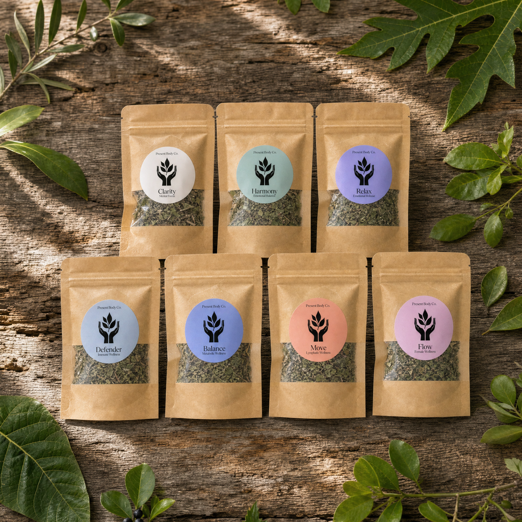 Seven small kraft paper pouches of loose-leaf tea arranged on a rustic wooden surface with green leaves around them. Each pouch has a round label with a different pastel color and a black leaf logo.
