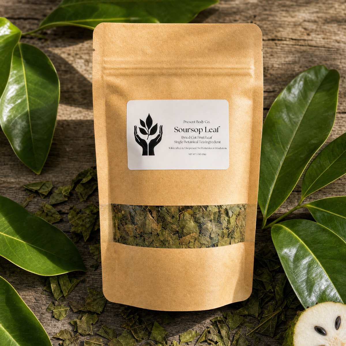 A kraft paper stand-up pouch labeled 'Soursop Leaf' by Present Body Co., surrounded by green leaves and scattered dried leaf pieces on a rustic wooden surface.