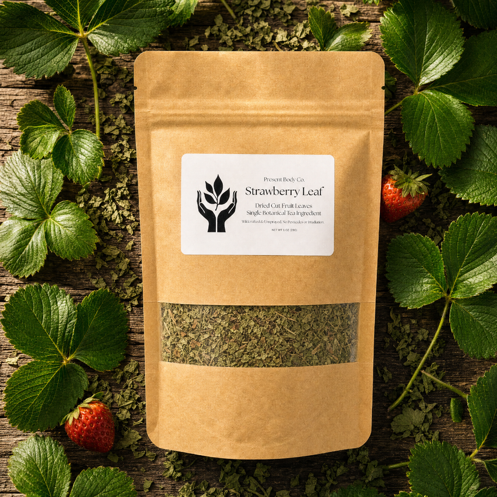 A kraft paper stand-up pouch labeled 'Strawberry Leaf' by Proud Root Co, placed on a rustic wooden surface surrounded by fresh green leaves and a few strawberries.