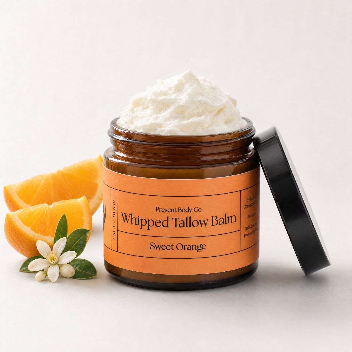 An open amber jar of Presenta Body Co. Whipped Tallow Balm in Sweet Orange, filled with whipped off-white balm and shown with its black lid leaning against it.