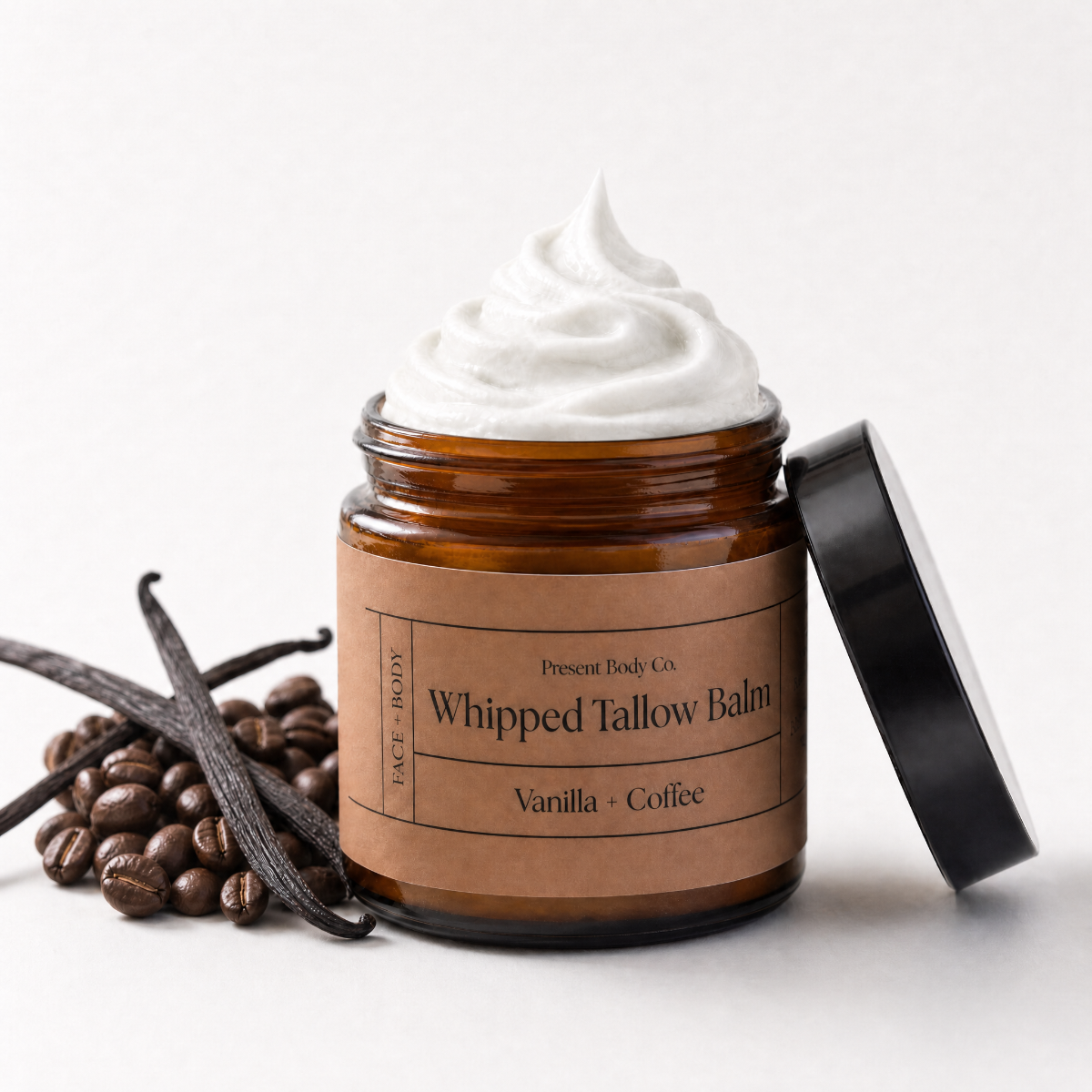 An open amber glass jar of whipped tallow body balm with a black lid leaning against it, topped with a swirl of white balm. The label reads 'Present Body Co.